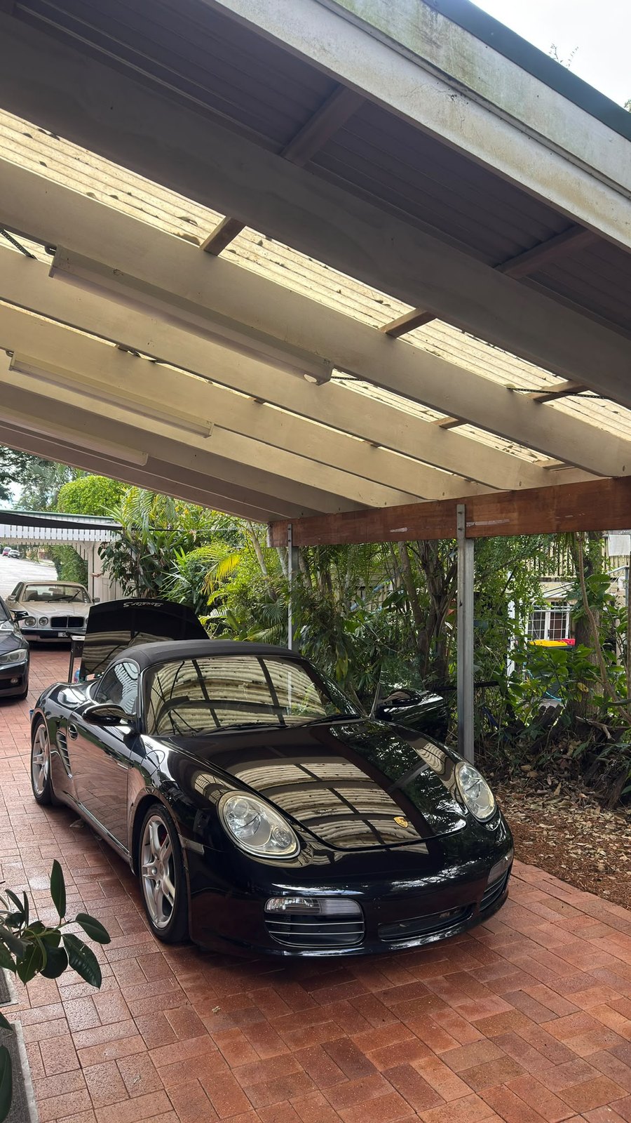 Freshly washed black convertible under a carport, paint reflecting the roofline