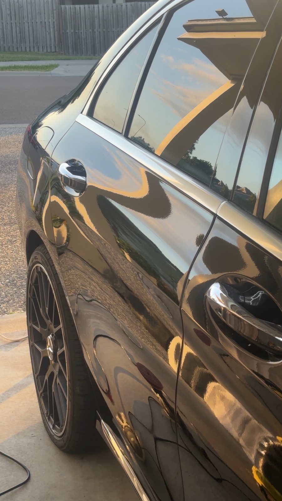 Close-up of a black car door with deep gloss reflecting the evening sky
